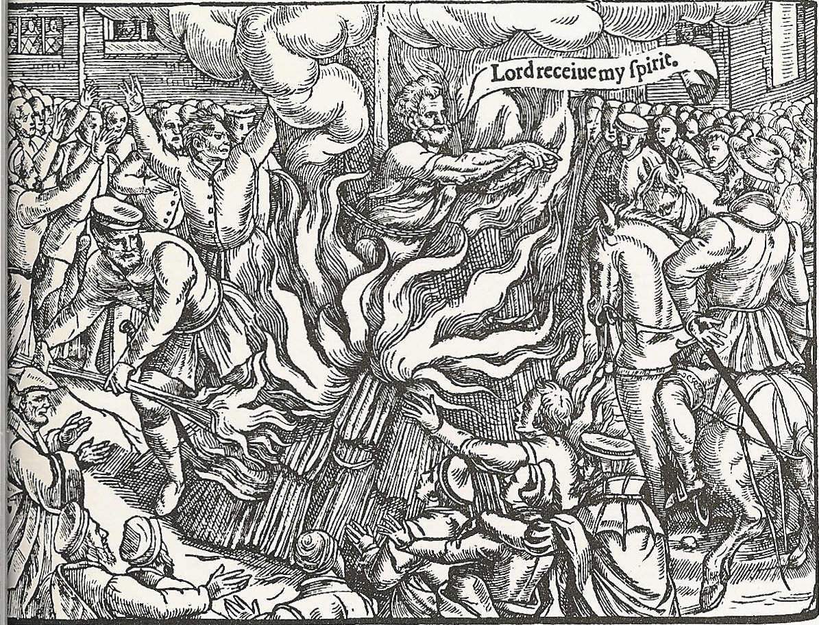 Woodcut of a bearded man in a long gown chained to a stake amid flames, with a speech scroll above him and onlookers