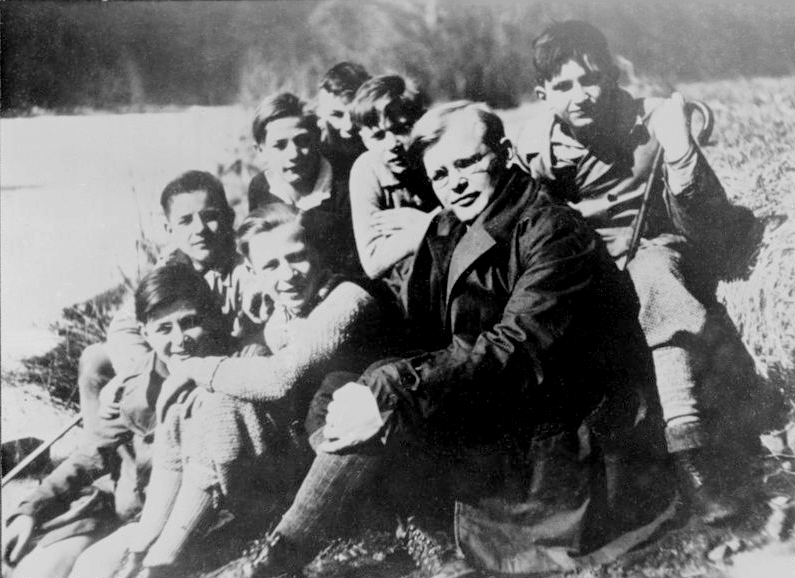 Black and white group photograph of a young man in a suit standing among a group of teenage boys outdoors
