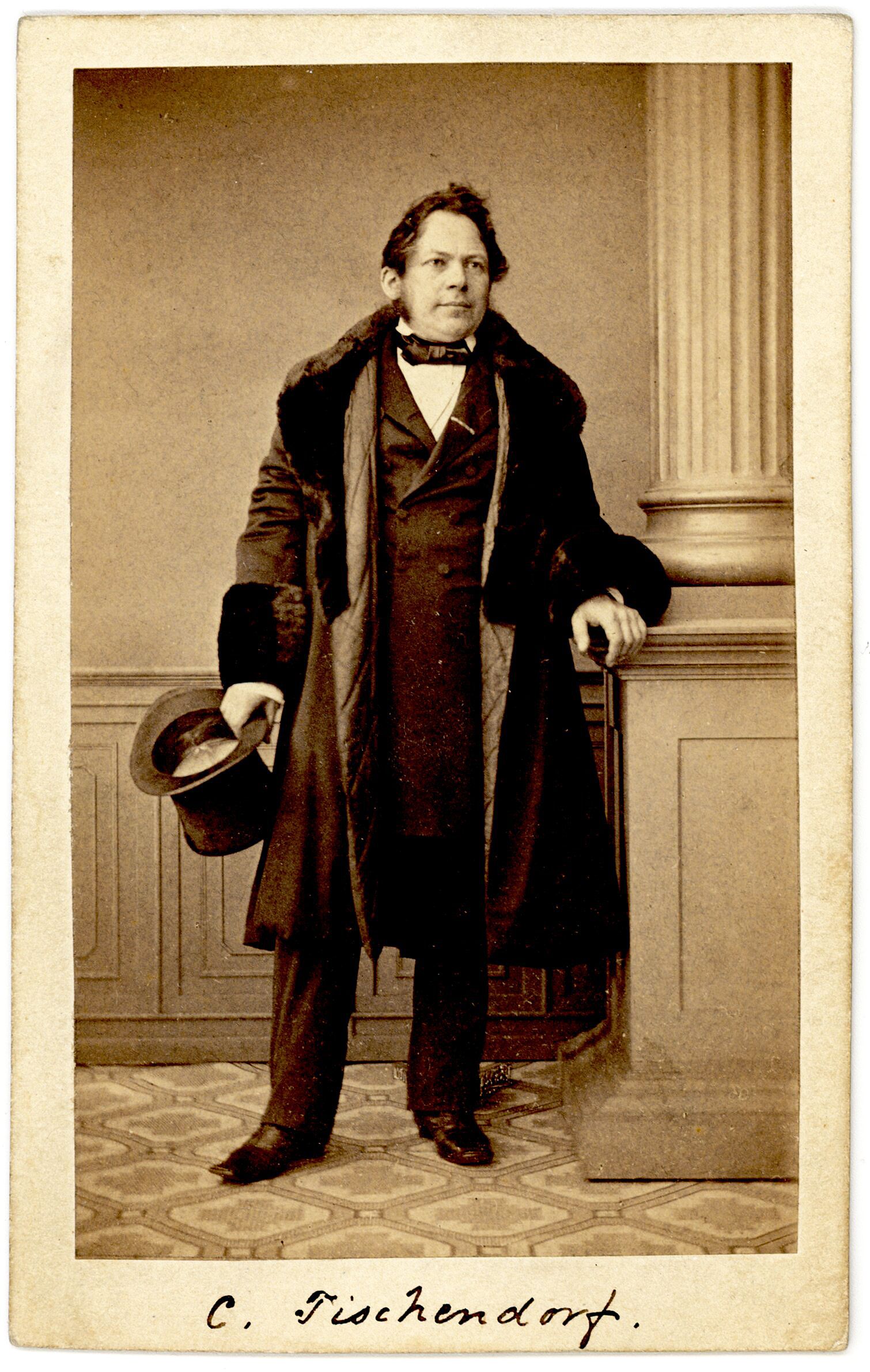 Studio portrait photograph of a middle-aged man with short hair and side whiskers, wearing a dark coat with a decoration on a ribbon at his neck