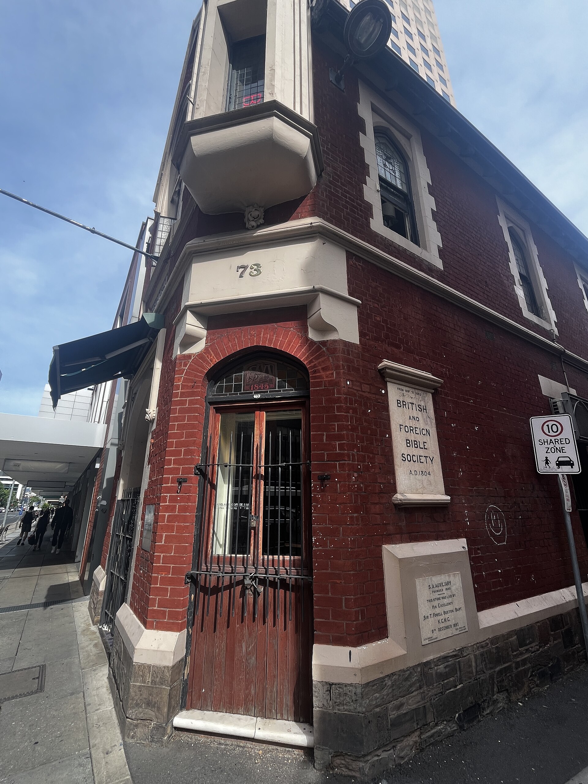 Street view of a two-storey stone building with arched windows and a sign reading The British and Foreign Bible Society, photographed in daylight