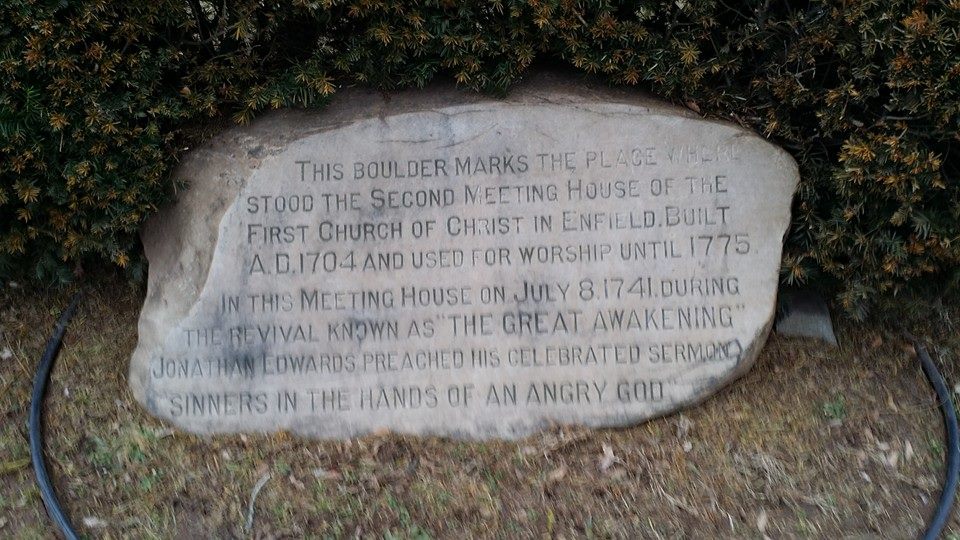 A stone monument with a carved inscription standing beside a road, with trees and grass around it