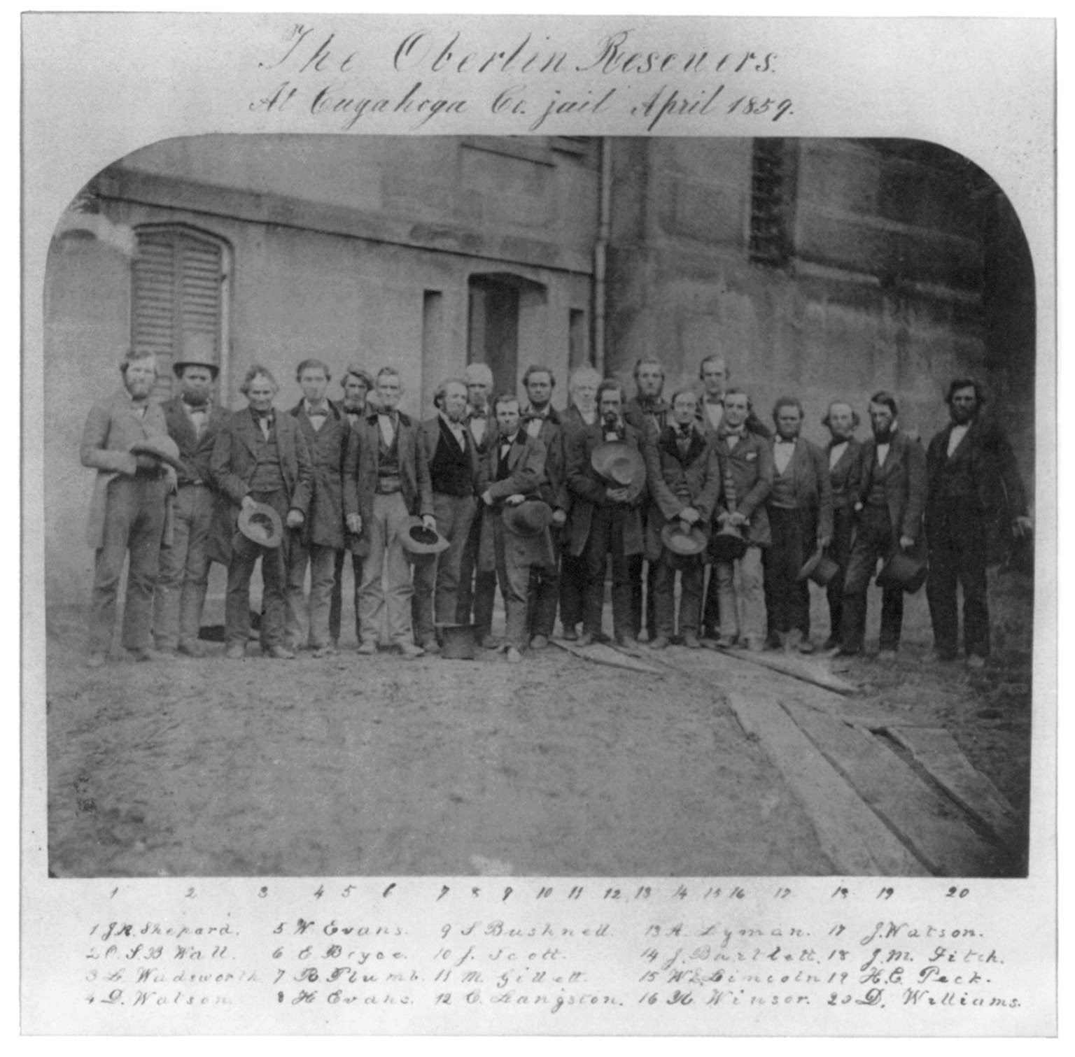 Old albumen group photograph of about twenty men in dark nineteenth century coats, posed together in rows