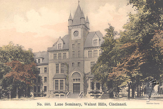 Old photograph of a plain three-story brick building with rows of windows and a small cupola, standing among trees
