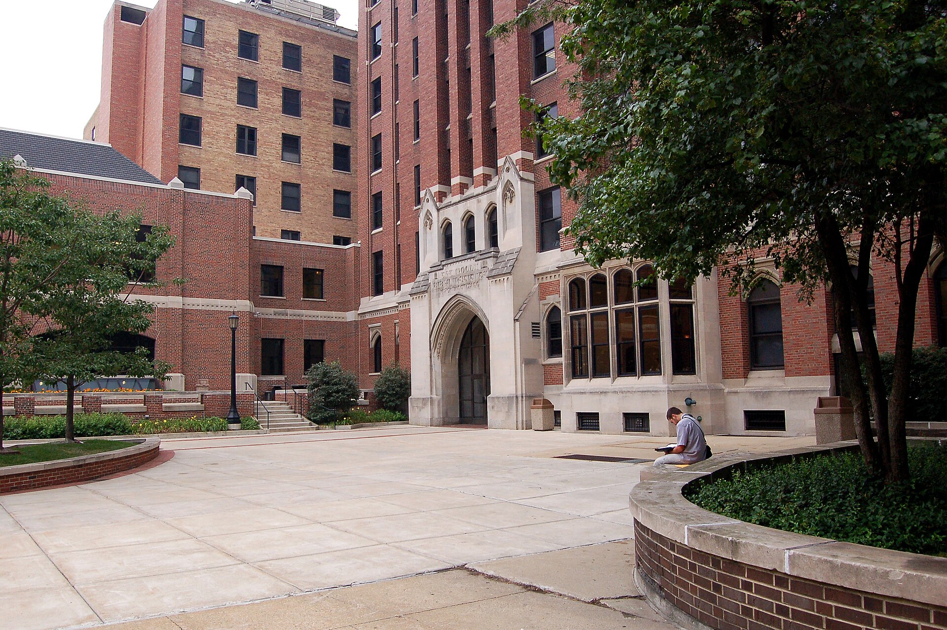 A paved plaza on the Moody Bible Institute campus in Chicago, with tall red brick buildings, an arched entrance, planters and trees