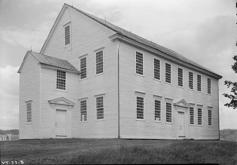 Black and white photograph of the Rockingham Meeting House, a plain two-story white clapboard meeting house with rows of windows and two small entrance porches