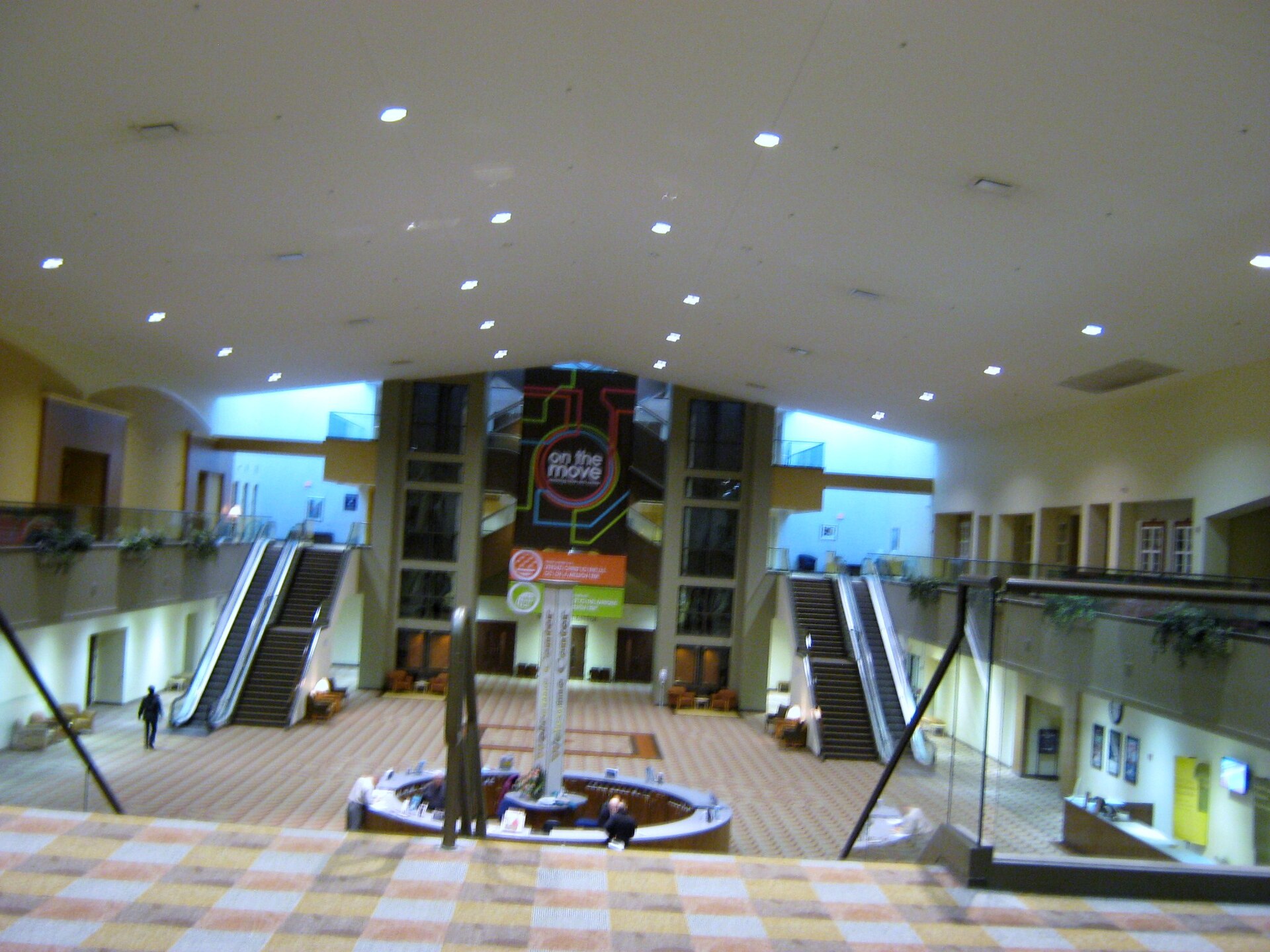 A large two-level church lobby with escalators, an upper walkway, tall windows and a round feature at the center of the floor