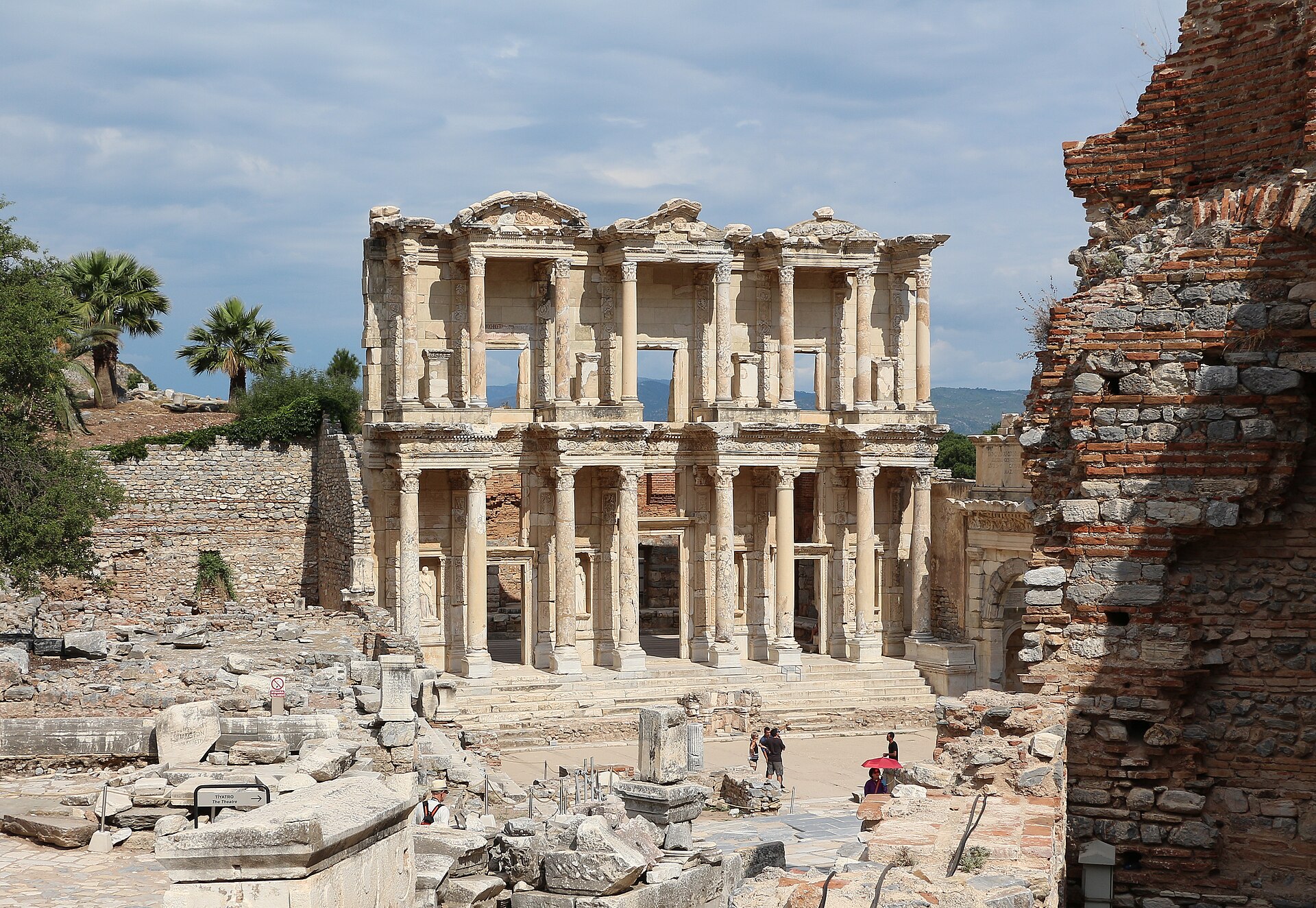Two-story marble facade of an ancient Roman library with columns, statues in niches and a wide stairway, under a blue sky
