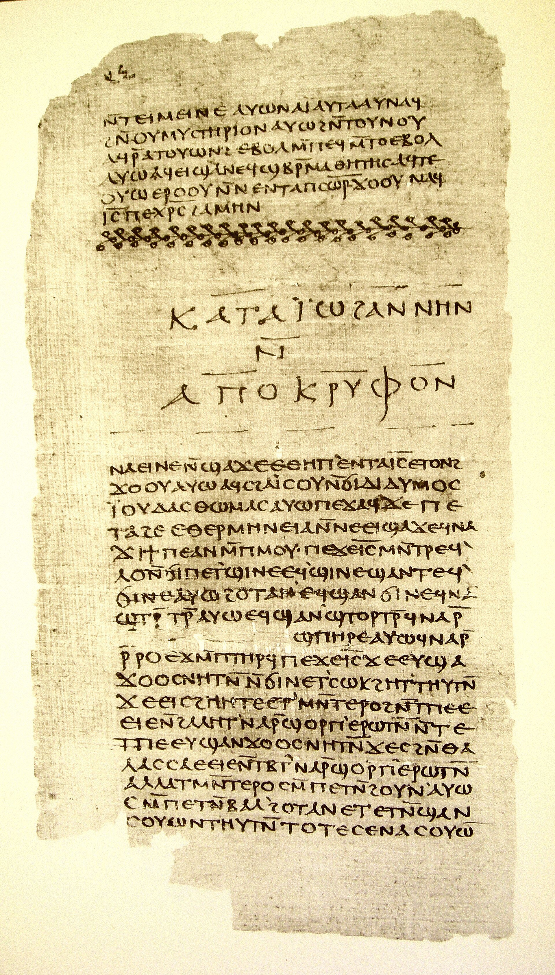 A tall brown papyrus page densely written in two blocks of Coptic letters, with a decorated title line between them