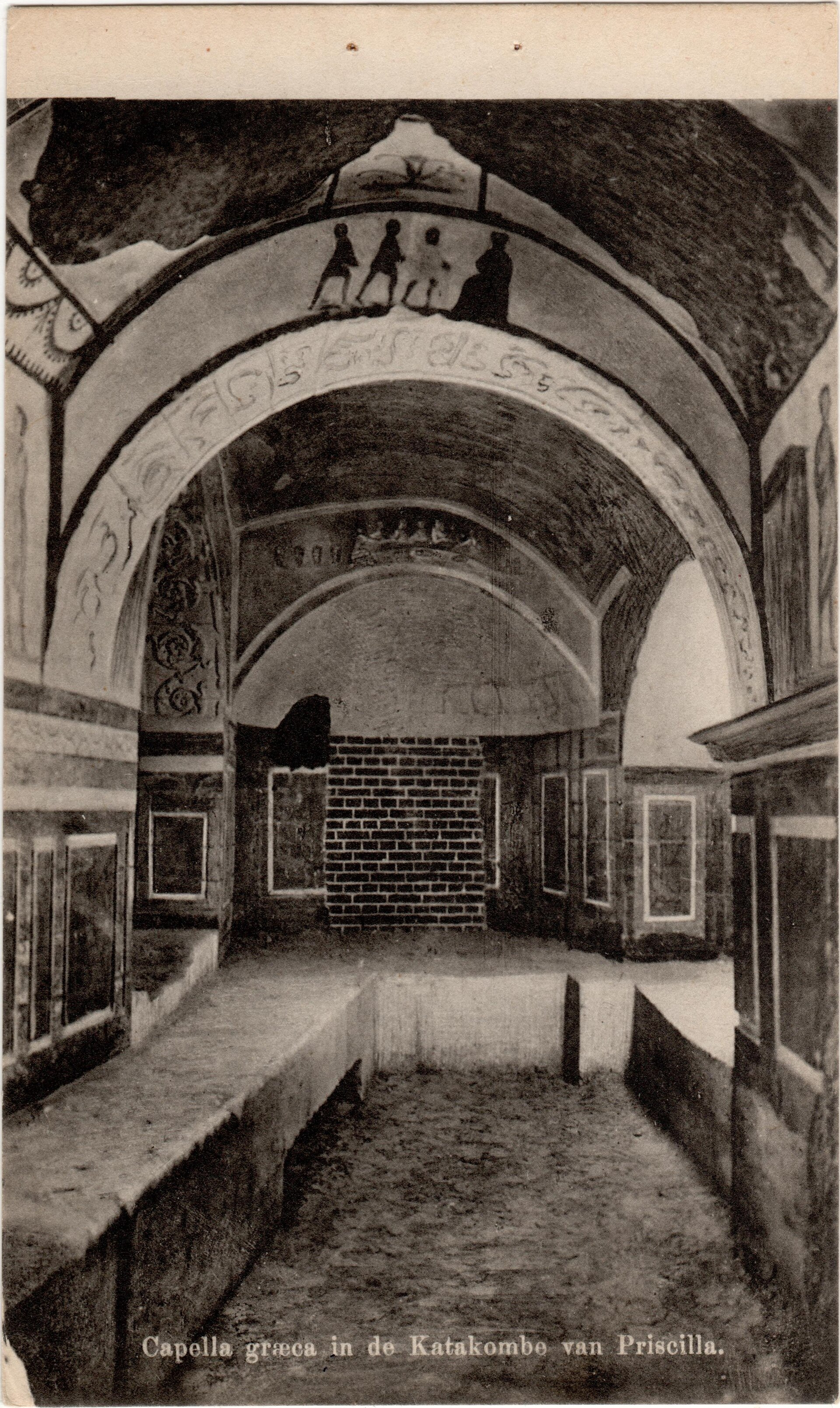 A black and white postcard photograph of an underground chamber with arched ceilings and faded wall paintings, lit from the front