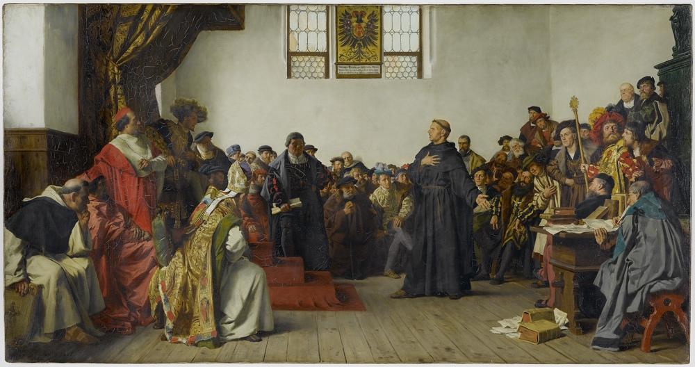 A large crowded painting of a hall in which a monk in a dark habit stands with one hand raised before a young seated ruler on a dais, surrounded by nobles, clergy and soldiers