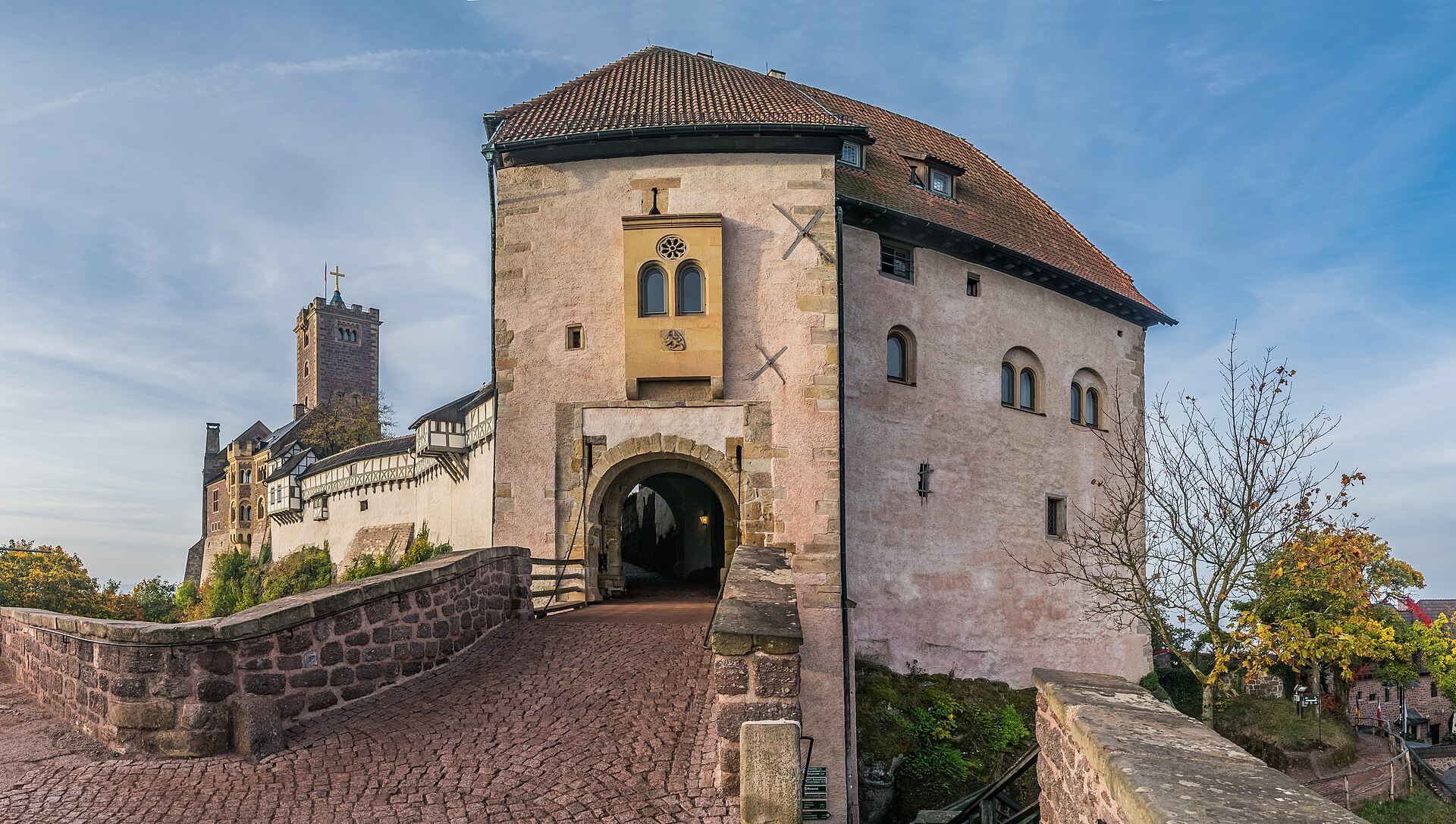 A long medieval castle with half-timbered upper stories and a square stone tower standing on a wooded ridge under a pale sky