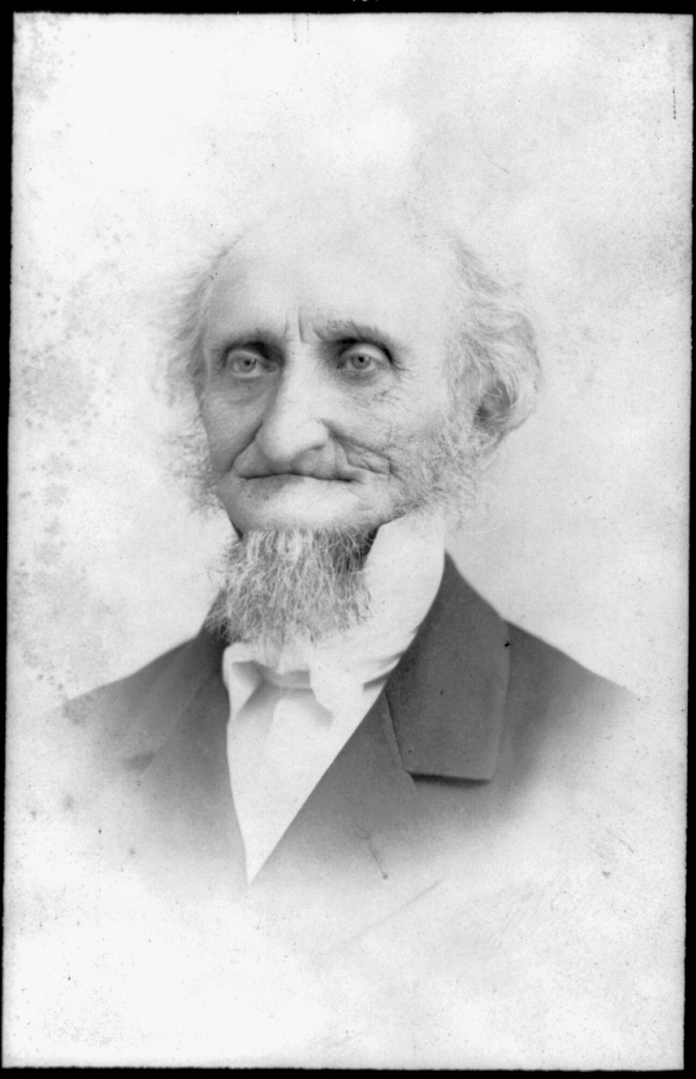 Black and white photograph of a gray-haired man with a clean-shaven face, wearing a dark coat and white neckcloth