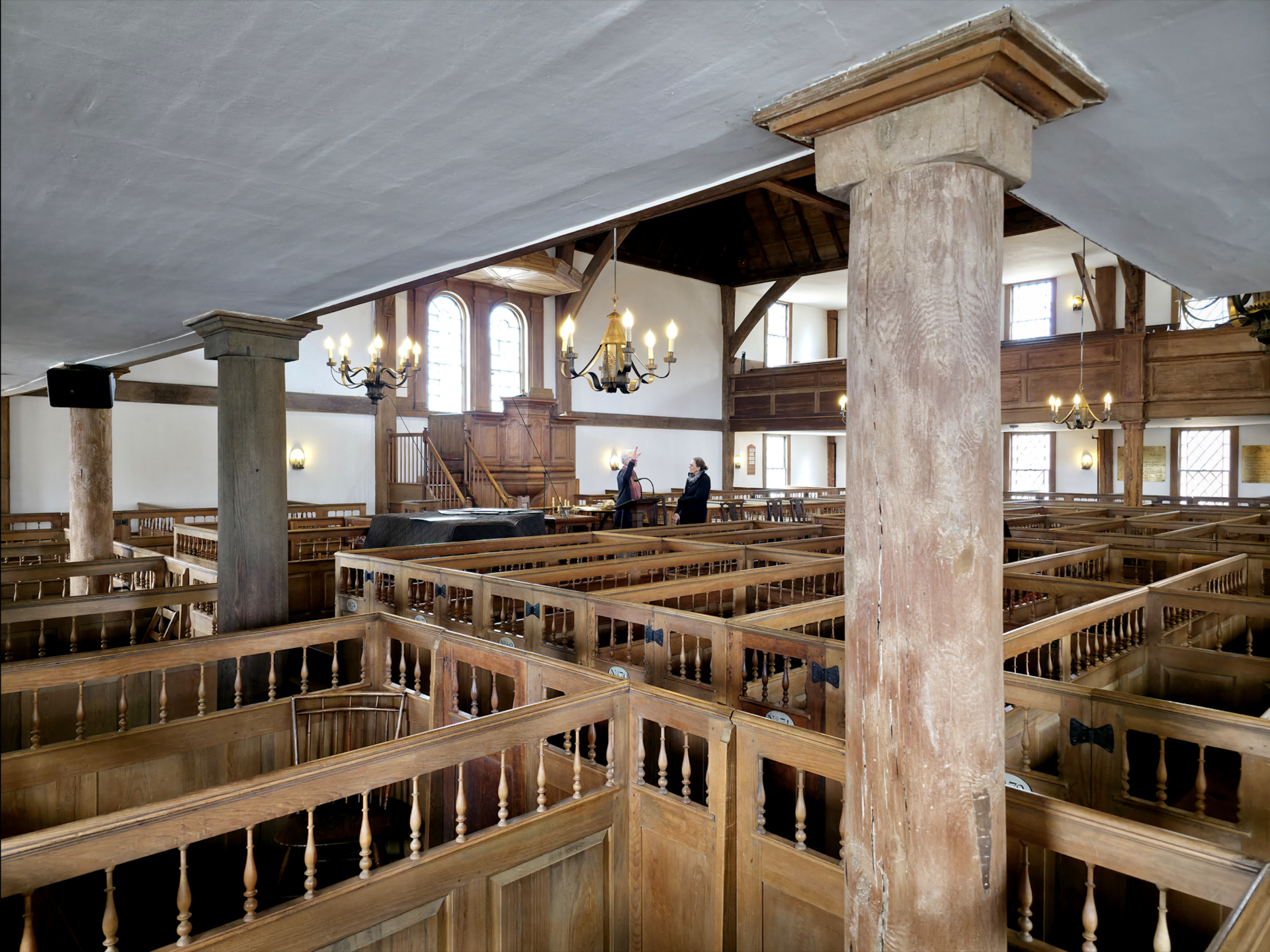 Interior of a wooden meetinghouse with rows of box pews, a raised pulpit on the far wall under a sounding board, a gallery along the sides, and exposed timber framing in the ceiling