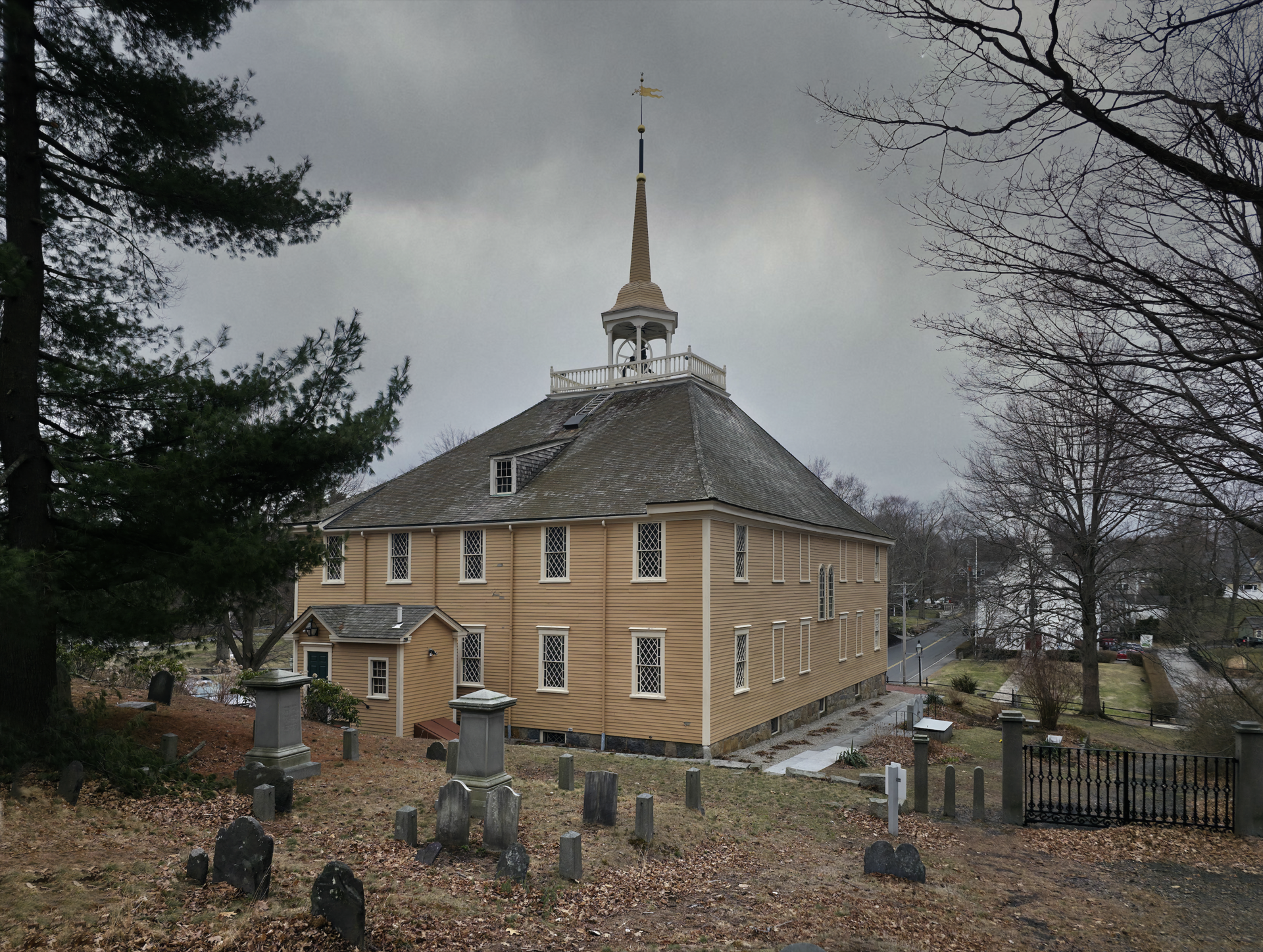 A plain white wooden meetinghouse with a hipped roof topped by a small open belfry, clapboard walls and tall windows, seen from the front lawn