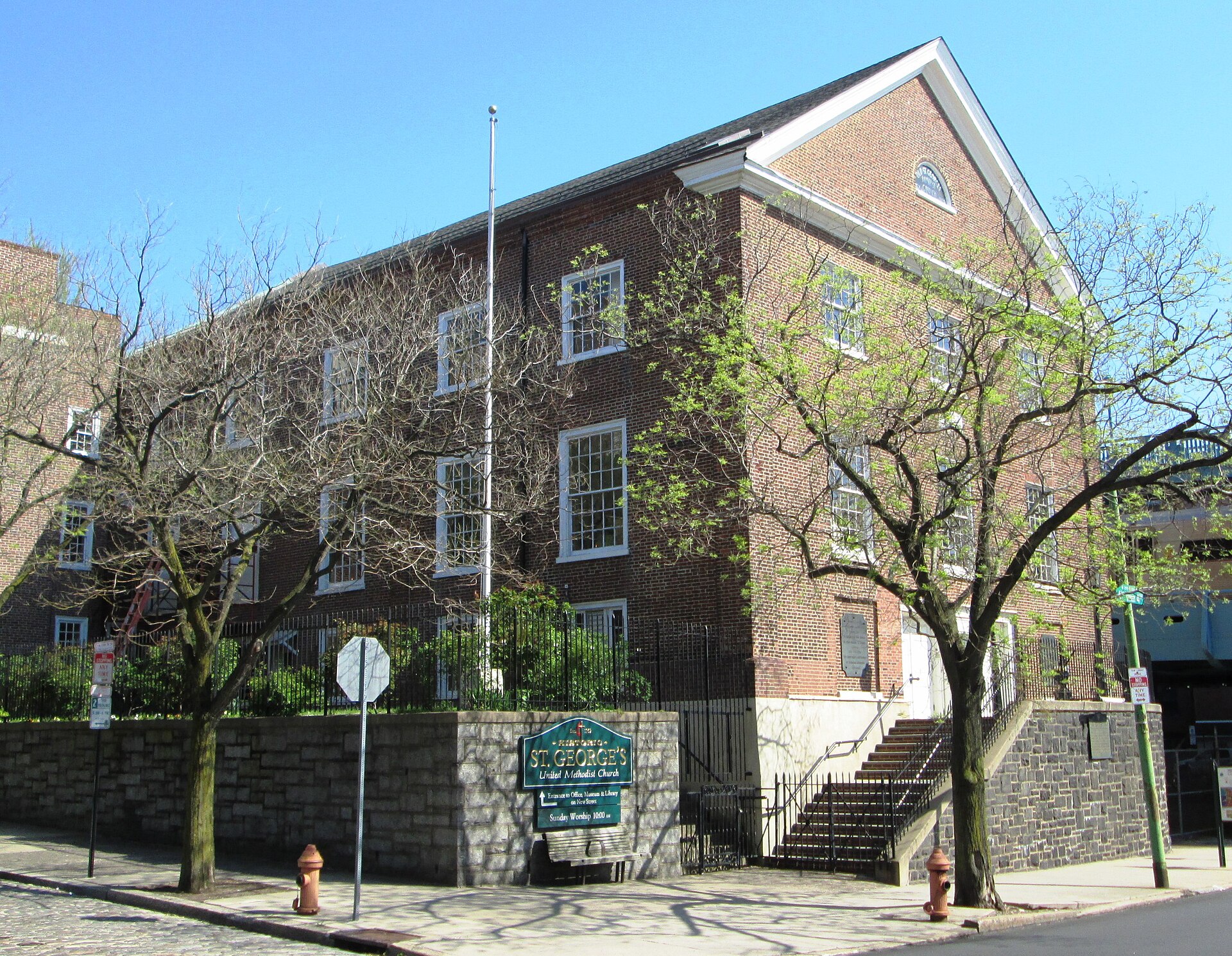 A plain red brick church with a gabled roof, white trim, arched windows and a small entrance porch on a city street corner