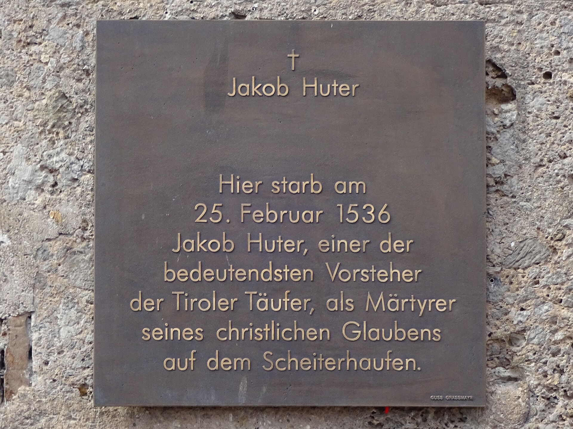 A bronze memorial plaque with German text mounted on a stone wall in the old town of Innsbruck
