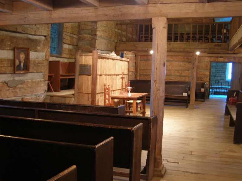 Interior of a log meeting house with plain wooden benches and log walls
