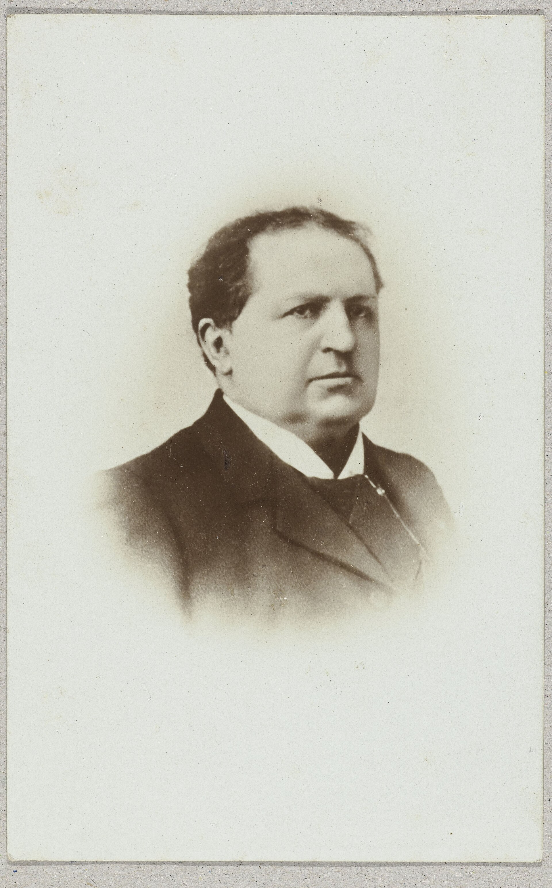 Black and white photographic postcard of an older man with a full white moustache and beard, in a dark coat, shown from the chest up