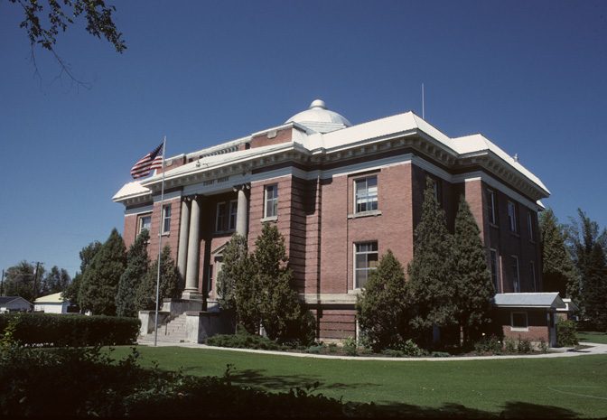 Red brick courthouse with a small dome, white columns at the entrance and an American flag