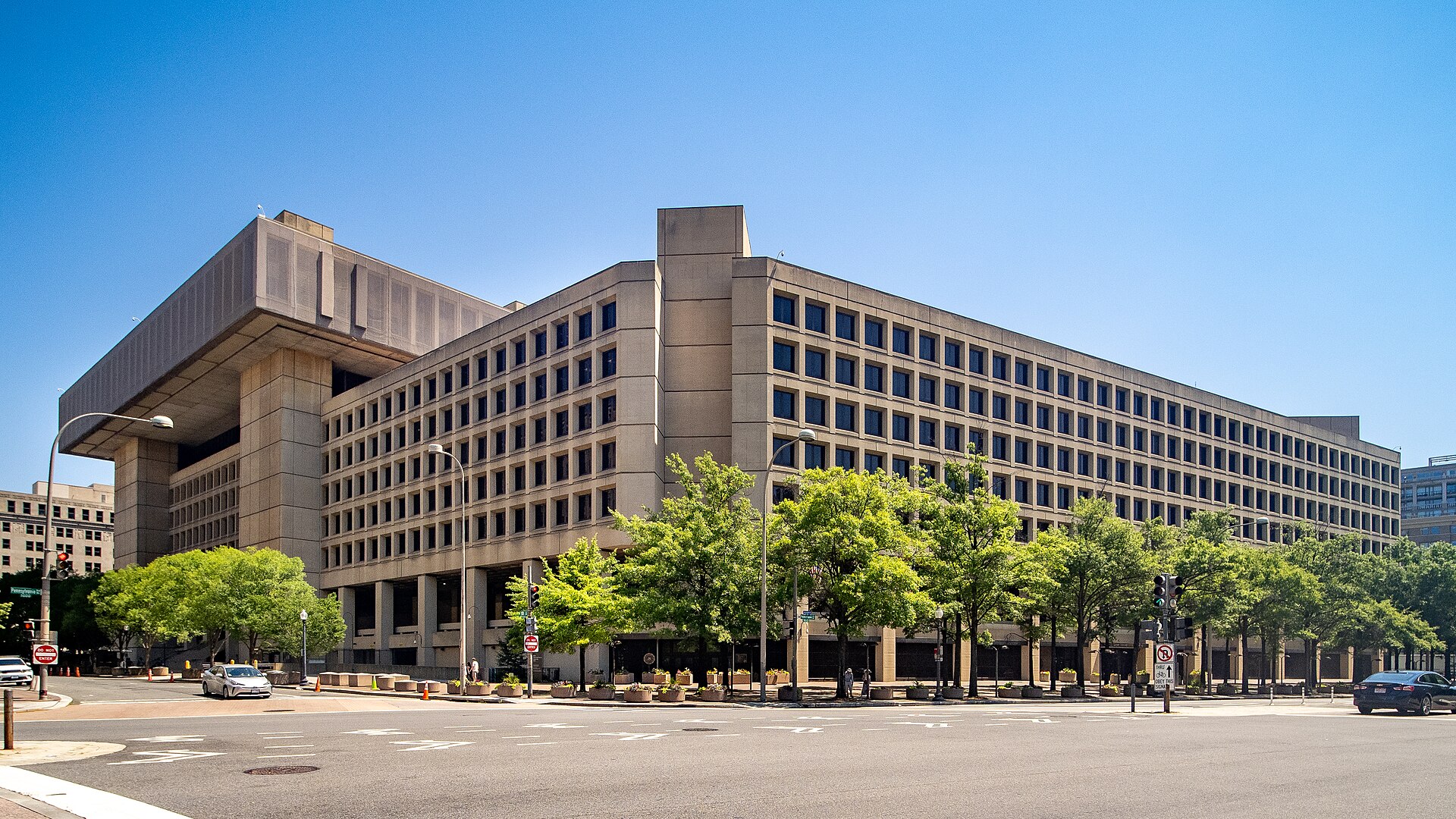 The J. Edgar Hoover Building, FBI headquarters, a large concrete office building on a Washington, D.C. street, photographed on a sunny day.