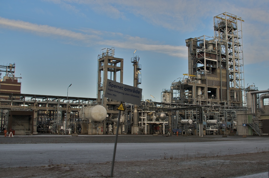 A large petrochemical plant with tall columns, storage spheres, pipe racks and a flare stack, seen from a distance.