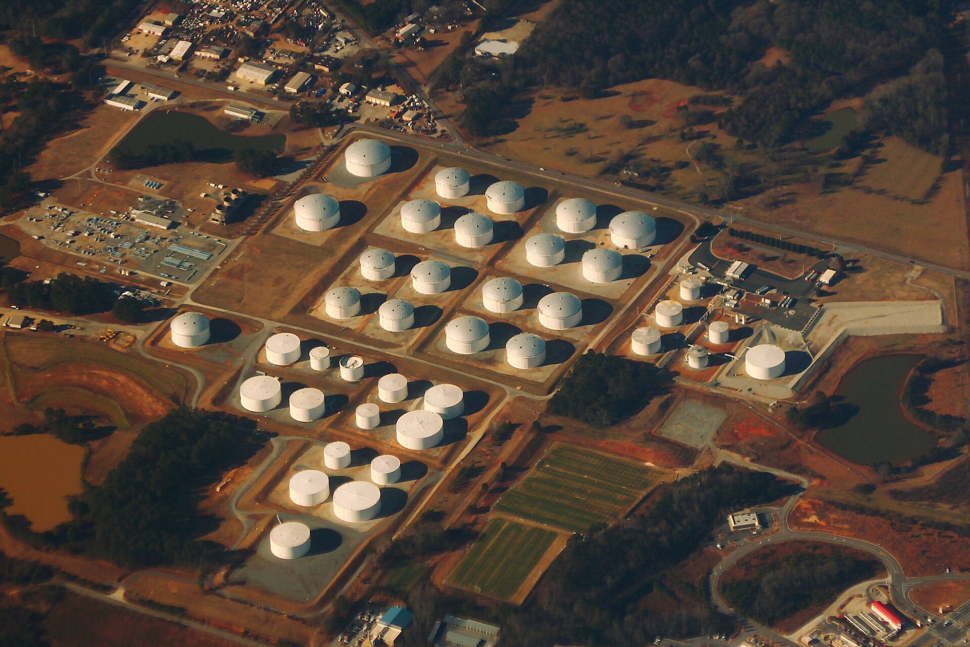 Rows of large white cylindrical fuel storage tanks at a tank farm, with pipes and catwalks, on a clear winter day.