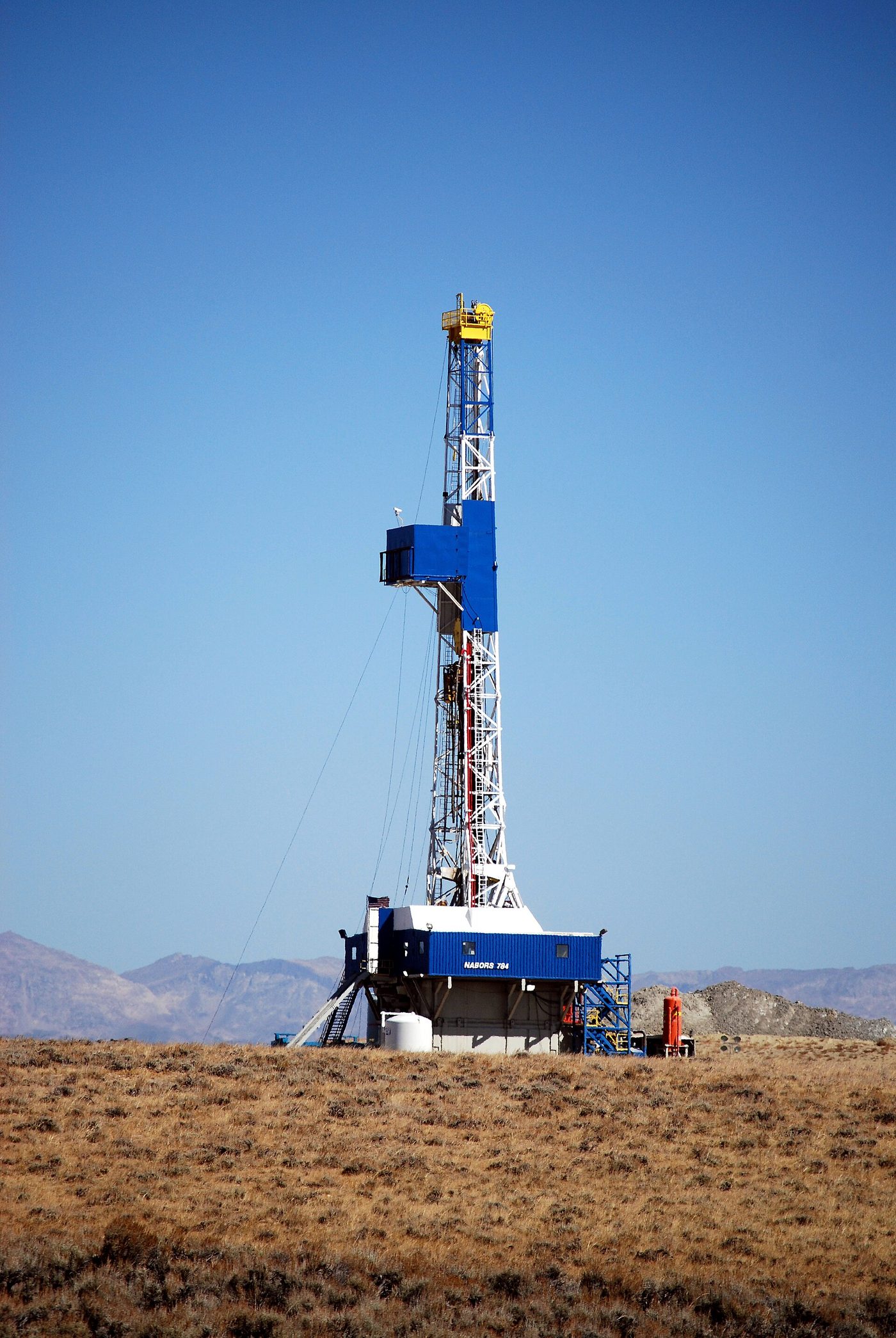 A tall oil and gas drilling rig standing on open sagebrush land in Wyoming