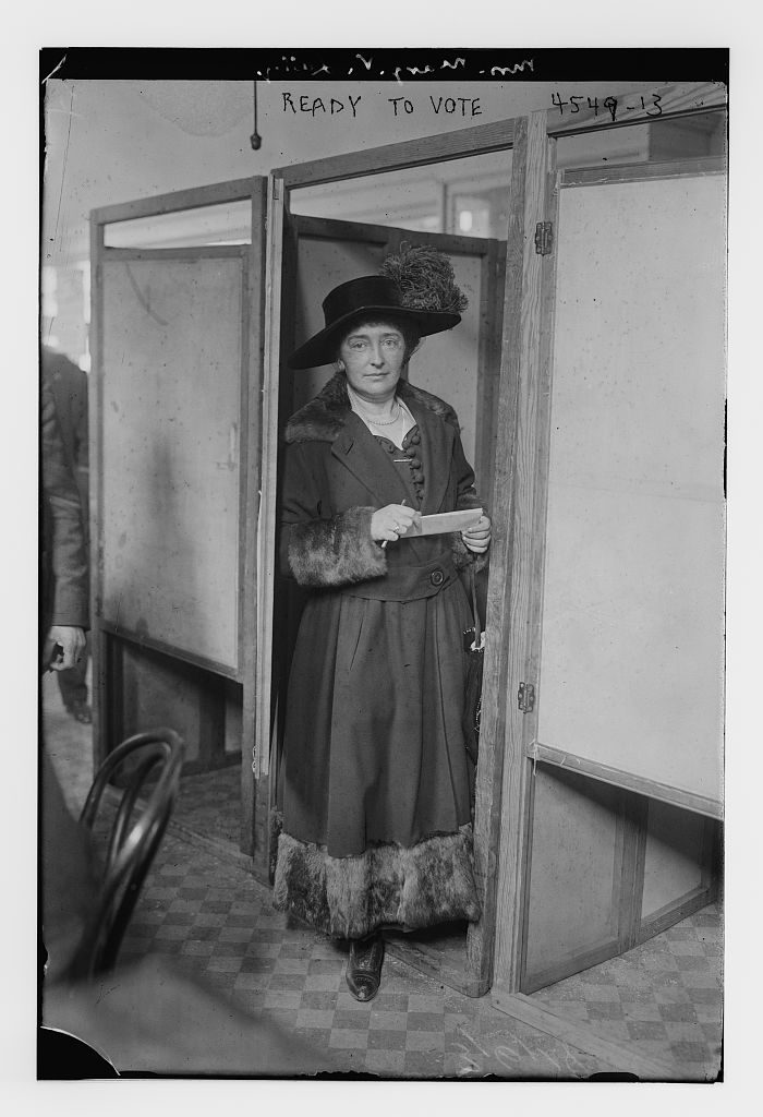 A woman in a long coat and hat standing outdoors in 1918, photographed as a voter