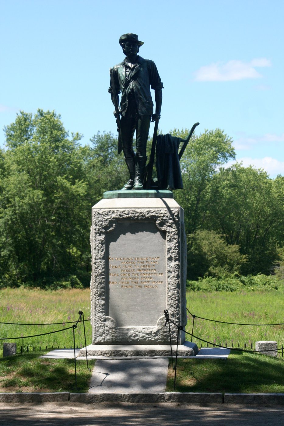 Bronze statue of a Minute Man holding a musket and standing beside a plow, on a granite pedestal near the Old North Bridge