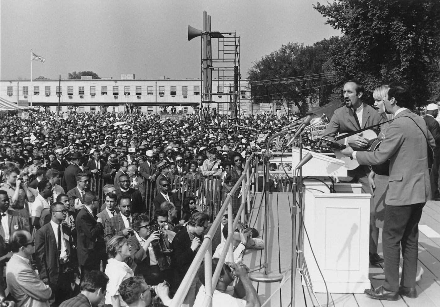 Folk singers Peter, Paul and Mary performing on a stage with microphones at the March on Washington, August 1963