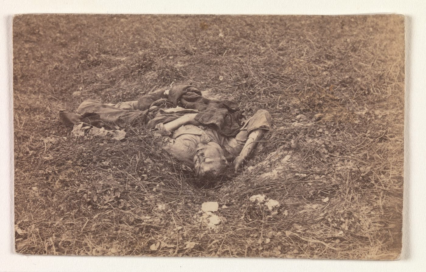 A photograph of a dead Confederate soldier lying on his back on open ground at Antietam, with a broken fence behind him