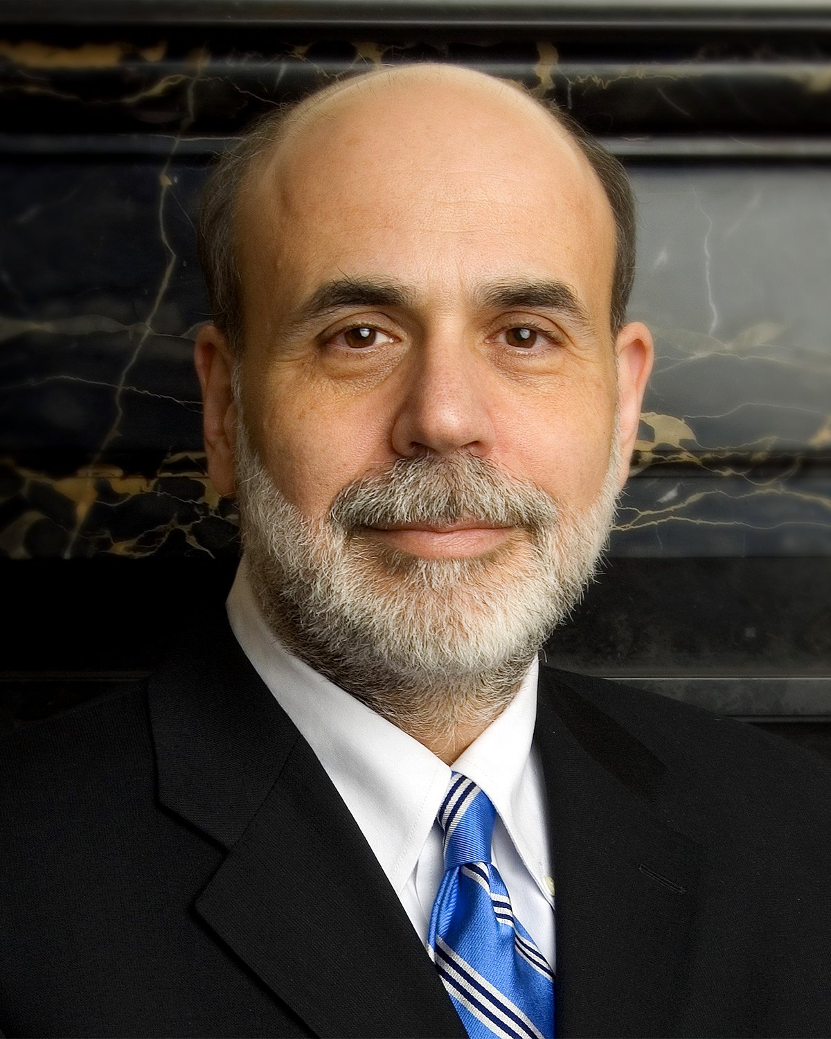Official portrait of Ben Bernanke in a dark suit before an American flag