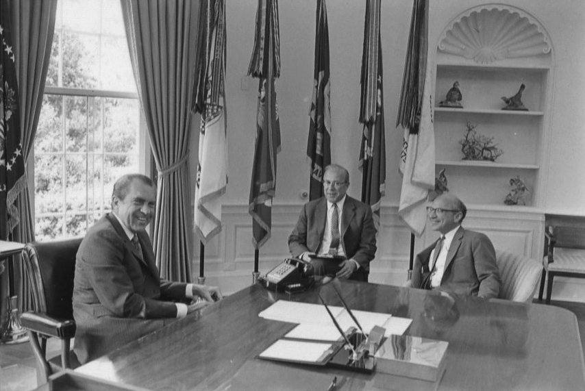 President Nixon seated at his Oval Office desk in a meeting with George Shultz and Milton Friedman, June 8, 1971
