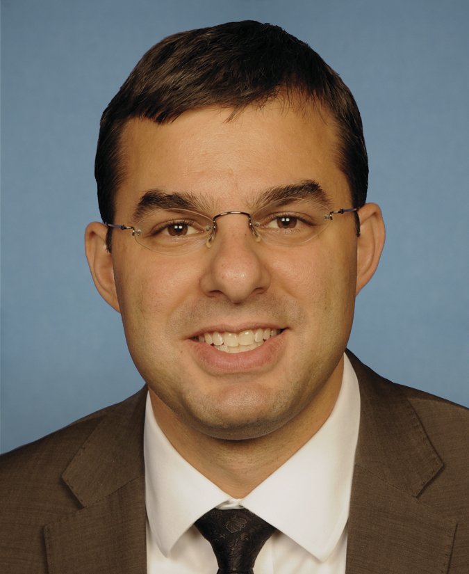 Official portrait of Congressman Justin Amash, a young man with short dark hair in a dark suit, in front of an American flag