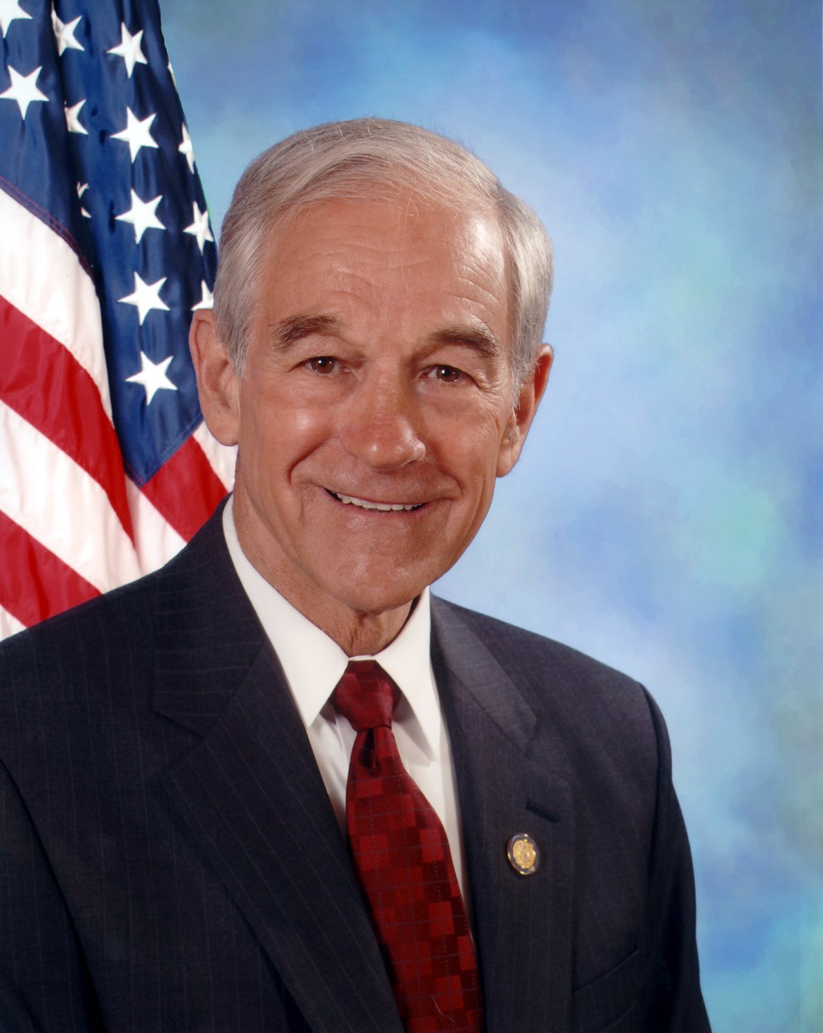 Official congressional portrait of Representative Ron Paul in a dark suit and red tie, with an American flag behind him