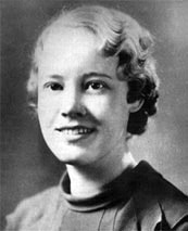Head-and-shoulders black and white portrait of a smiling young woman with short wavy hair, wearing a dark knit top