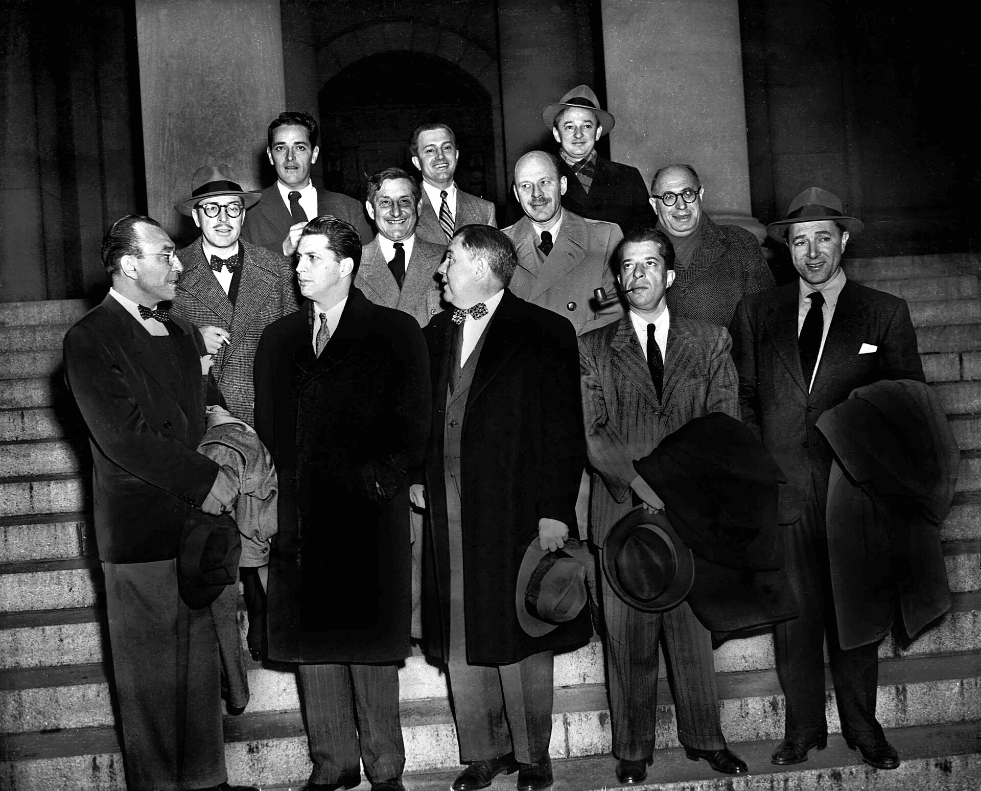 A group of men in overcoats and hats standing together outside a building