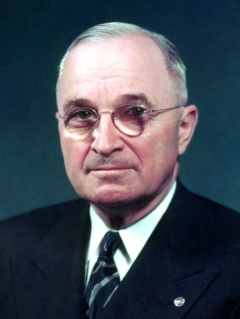 Formal portrait of President Harry S. Truman in a dark suit and tie, wearing round glasses, facing slightly to the side against a plain background