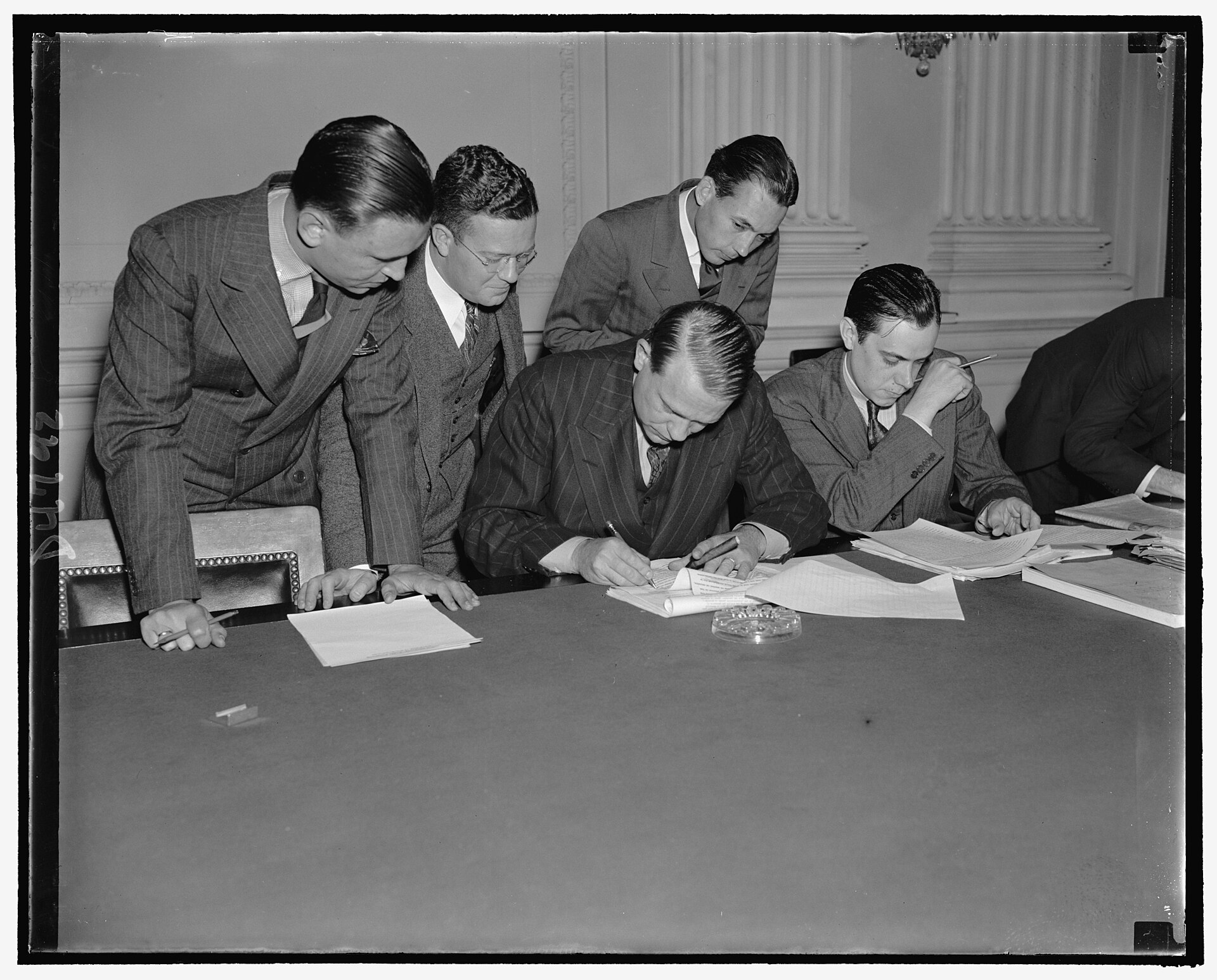 A man at a desk reading a typed statement while reporters around him take notes