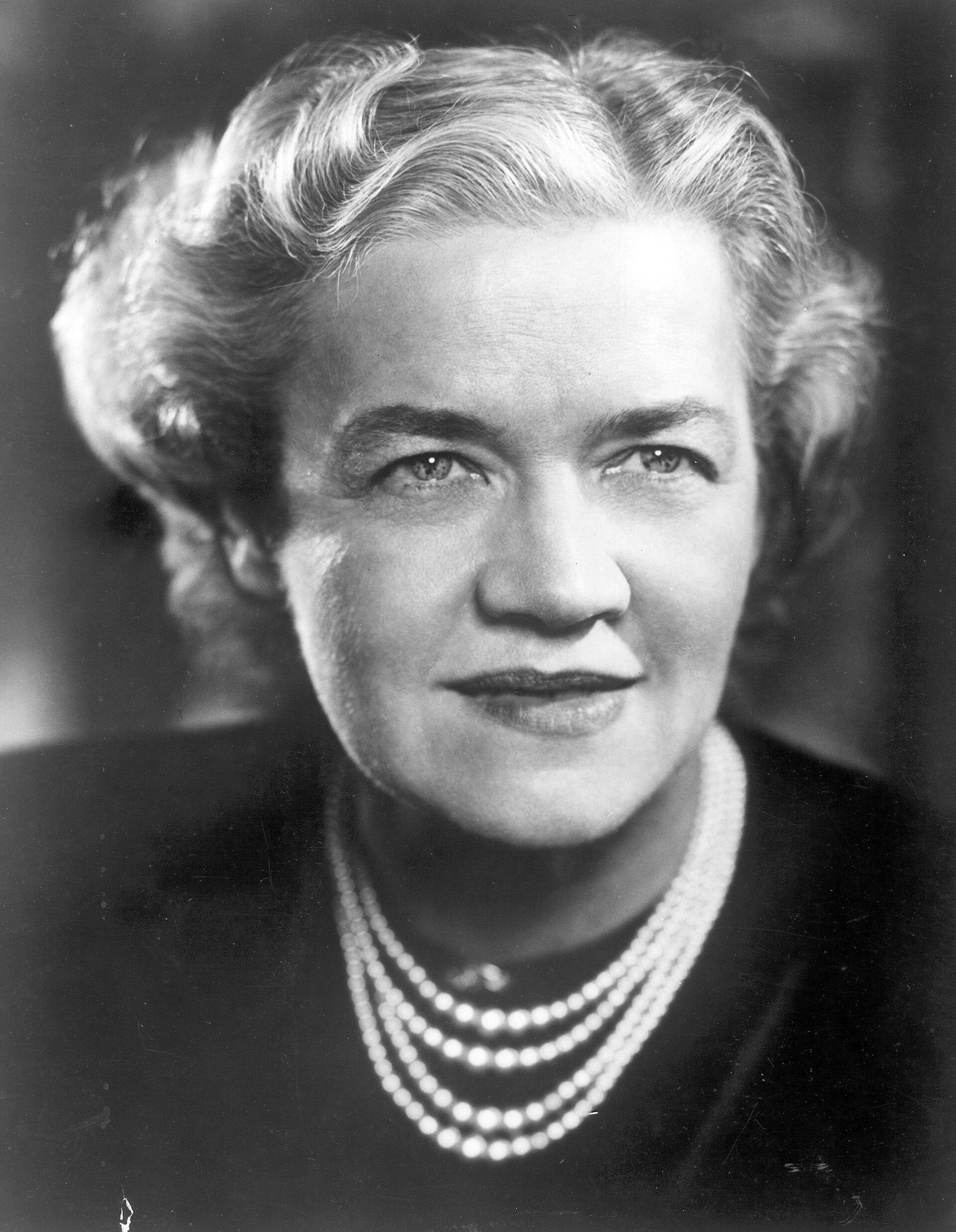 Black and white studio portrait of Margaret Chase Smith, a woman with wavy light hair, wearing a dark dress and several strands of pearls, looking toward the camera with a slight smile