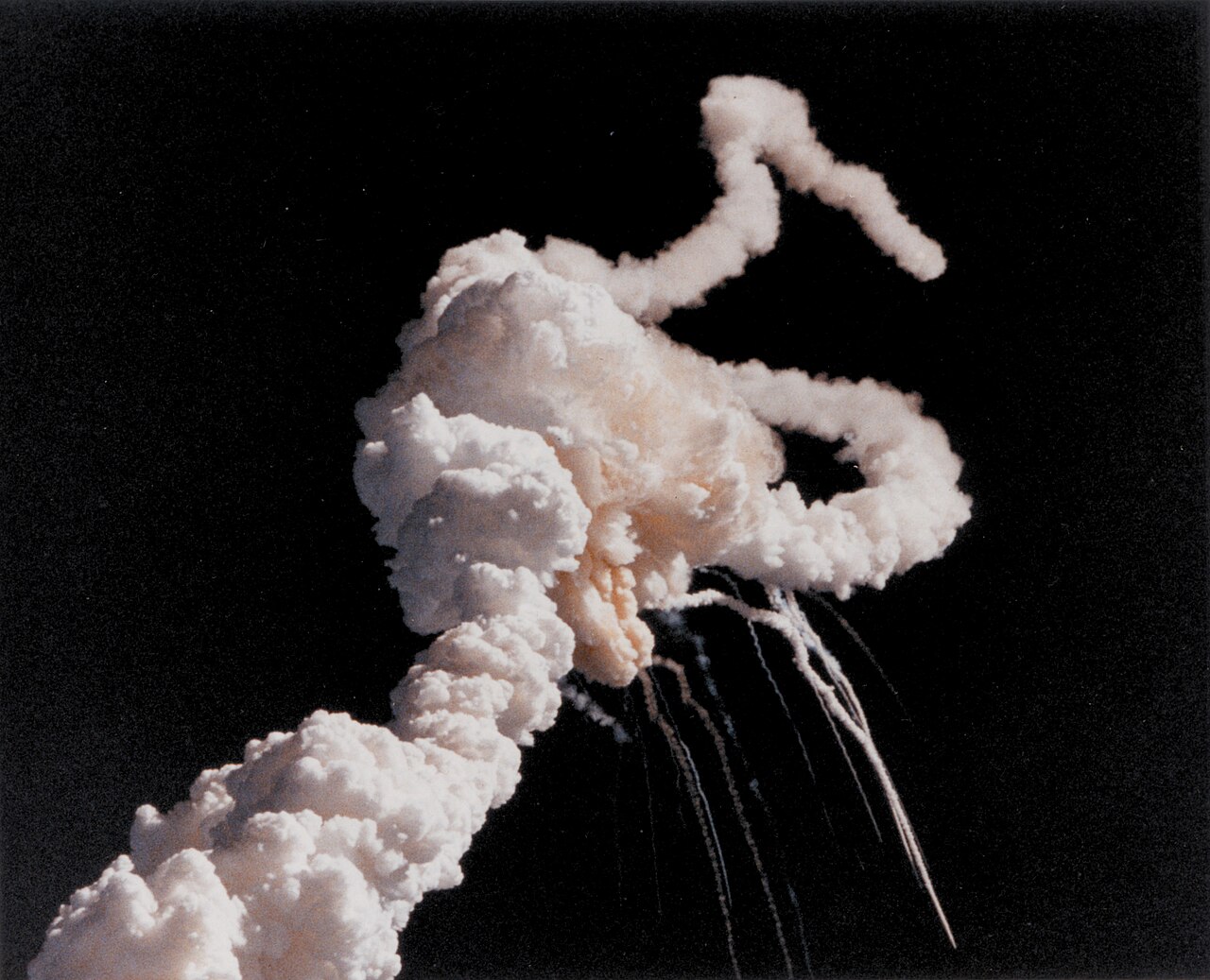 Photograph of the sky over Florida seconds after the Challenger shuttle broke apart, showing a large white cloud of gas with two curving trails of rocket exhaust
