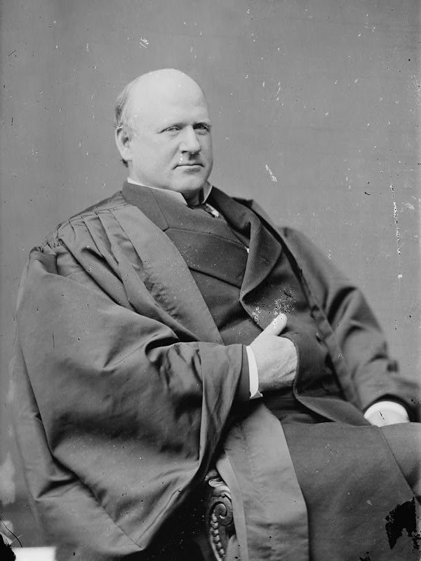 Black and white head and shoulders photograph of a balding man with a high forehead wearing a dark coat and bow tie