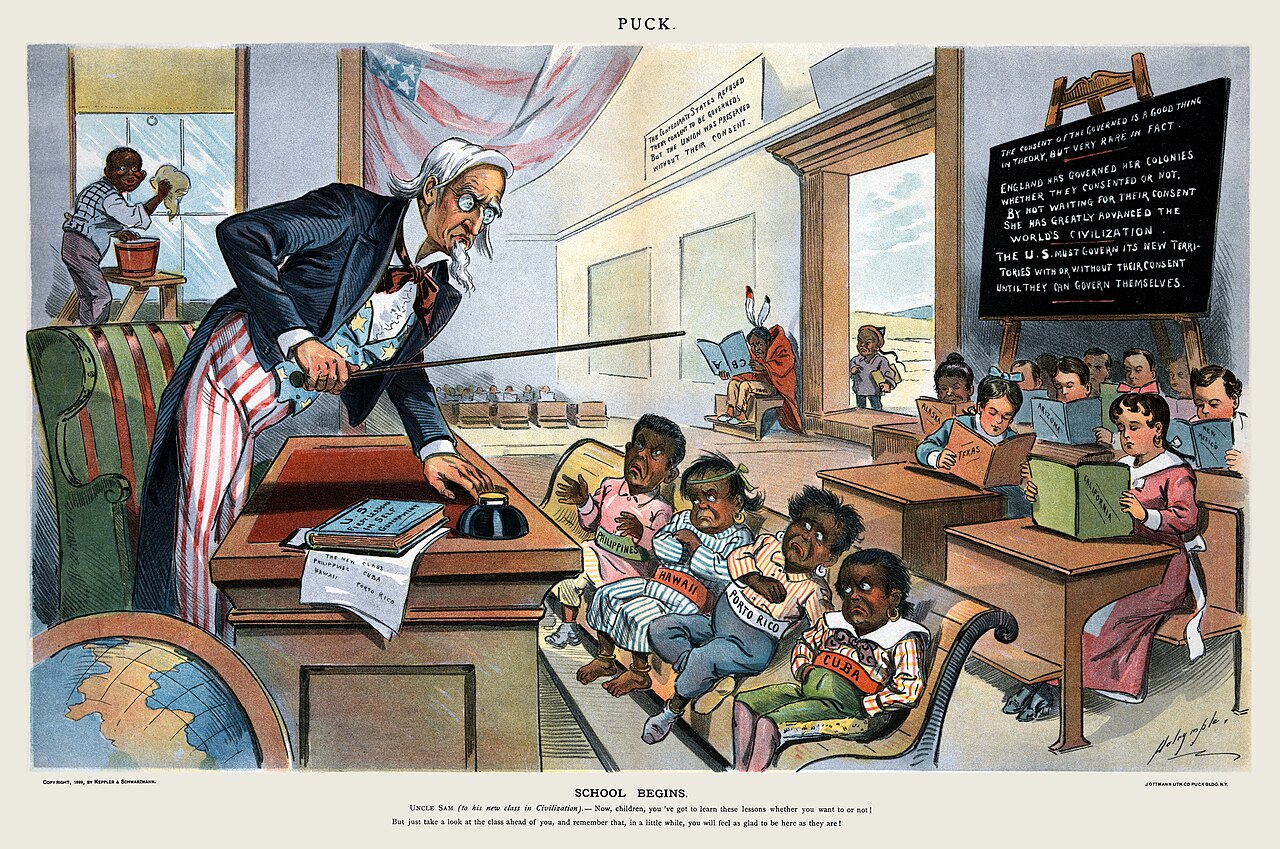 Color cartoon of Uncle Sam at a teacher desk facing four children labeled Philippines, Hawaii, Porto Rico and Cuba, with older students holding books named for states behind them and a blackboard with writing about consent of the governed