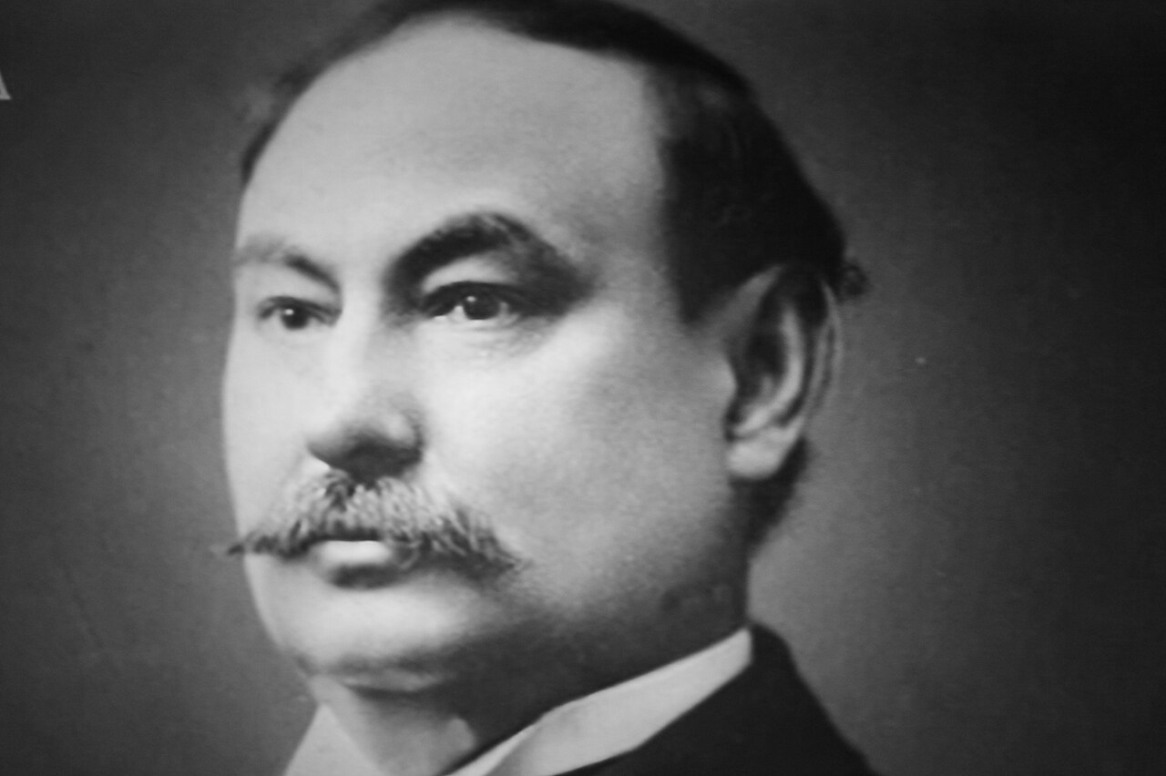 Black and white photograph of a balding middle-aged man with a mustache seated at a laboratory bench with glassware