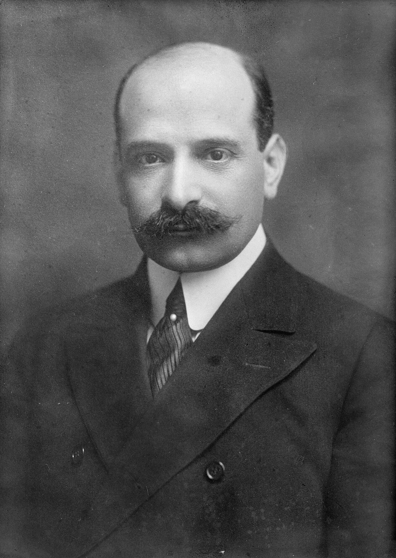 Black and white portrait of a man with a dark mustache and receding hair wearing a suit and tie