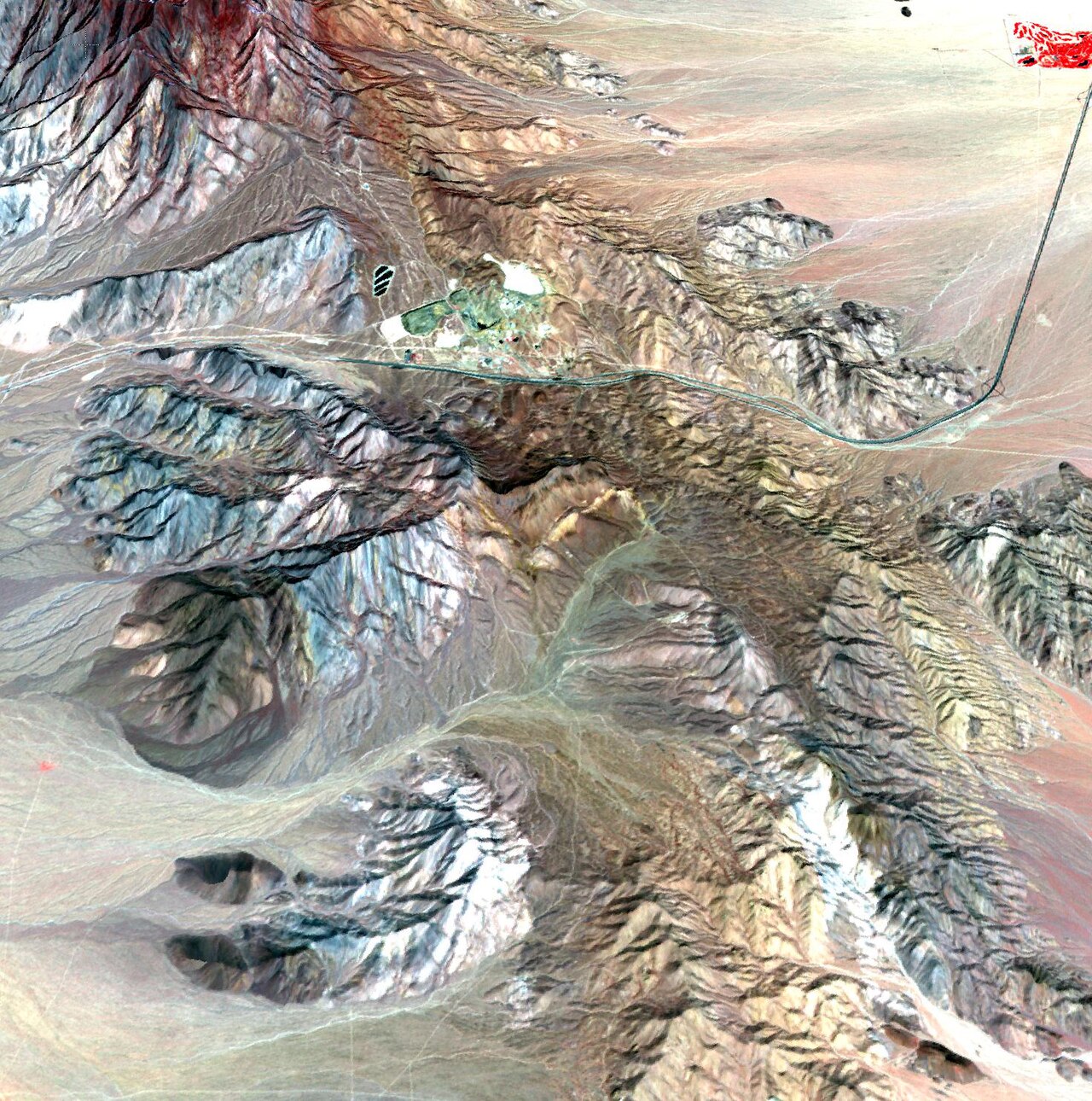 False-color satellite image of the Mountain Pass mine in the California desert, showing the open pit and tailings ponds among brown hills